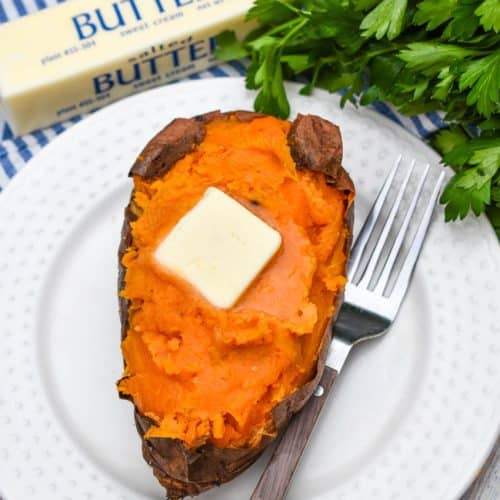 an air fryer baked sweet potato topped with a melting pat of butter on a small white plate with a fork resting on the side