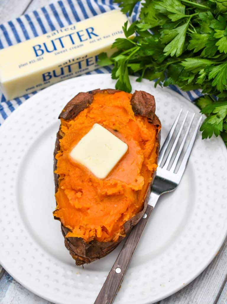 an air fryer baked sweet potato topped with a melting pat of butter on a small white plate with a fork resting on the side