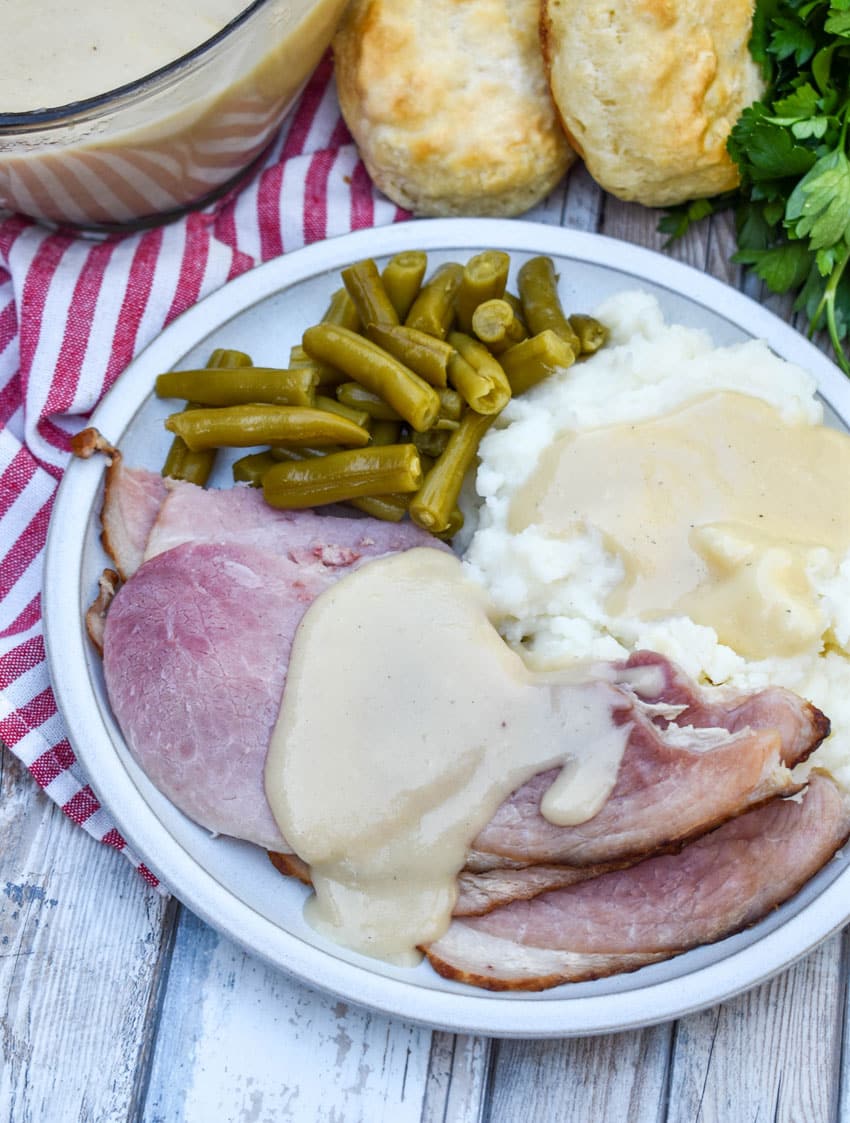 easy homemade gravy made from ham drippings over slices of spiral ham on a white plate