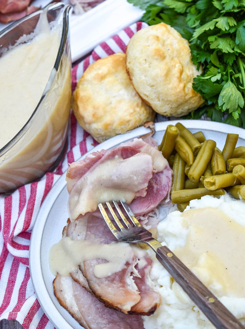 easy homemade gravy made from ham drippings over slices of spiral ham on a white plate
