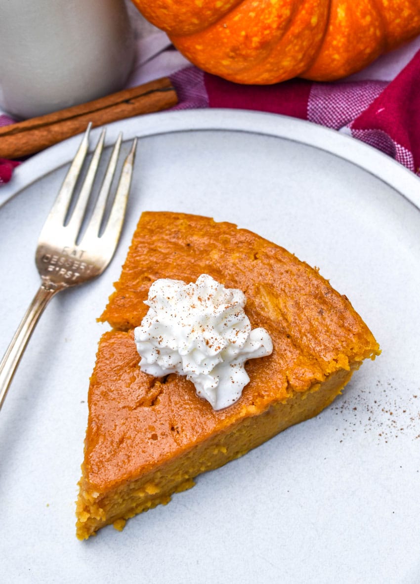 a sliced of impossible pumpkin pie topped with a dollop of whipped cream on a white plate with a silver fork resting on the side