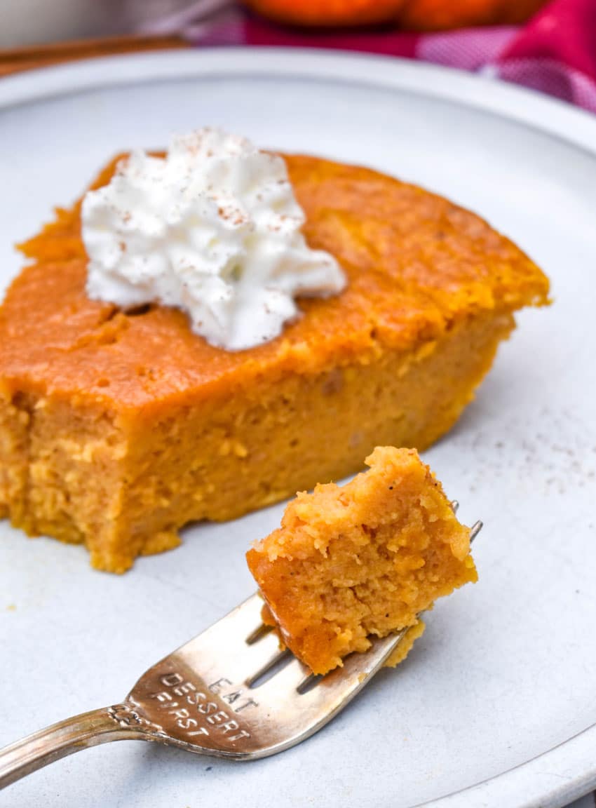 a silver fork holding a bite of crustless pumpkin pie resting on the edge of a white plate