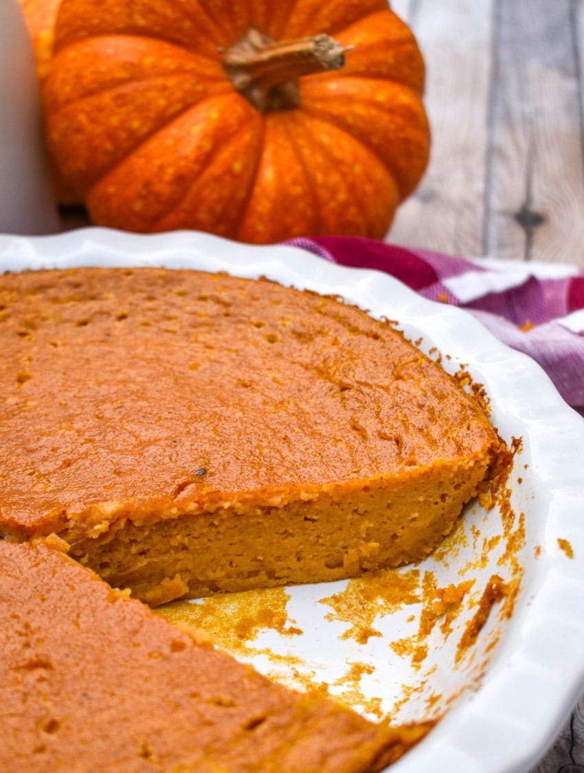 a crustless pumpkin pie in a white pie dish with a slice remove to show the filling