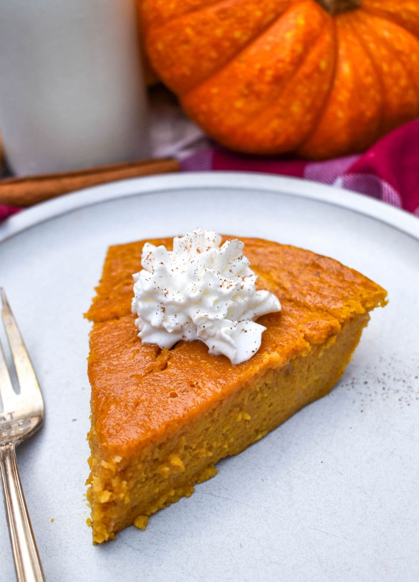 a sliced of impossible pumpkin pie topped with a dollop of whipped cream on a white plate with a silver fork resting on the side