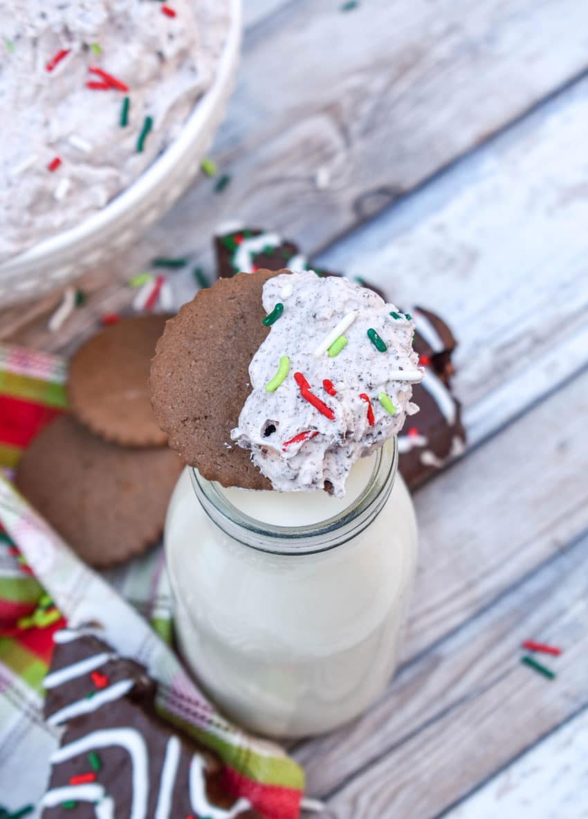 a hot cocoa flavored cookie topped with chocolate christmas tree cake dip resting on the edge of a glass of milk