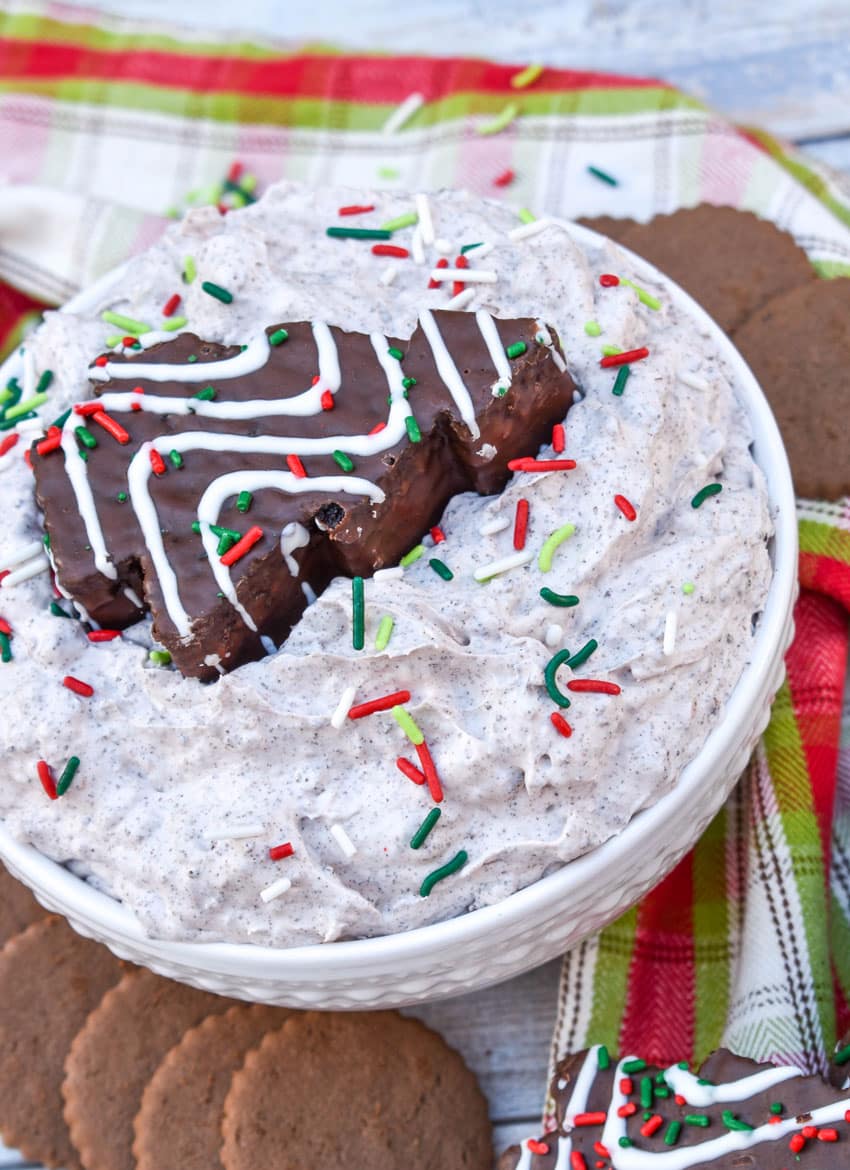 Chocolate Little Debbie Christmas Tree Cake dip in a white bowl topped with festive sprinkles and a dessert cake in the center