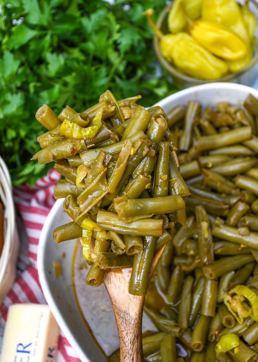 a wooden serving spoon holding up a scoop of mississippi style canned green beans