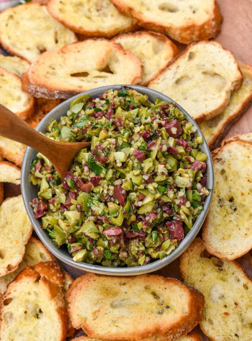 easy homemade olive tapenade in a small gray bowl surrounded by homemade crostini