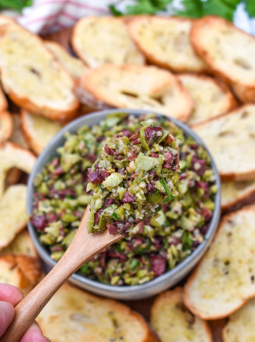 a wooden spoon holding up a scoop of easy olive tapenade
