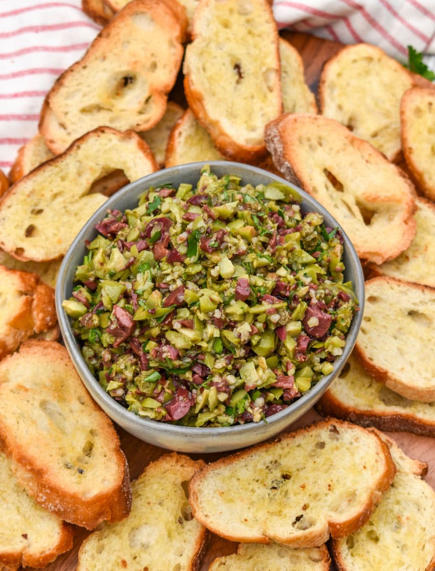 easy homemade olive tapenade in a small gray bowl surrounded by homemade crostini