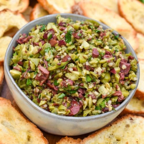 easy homemade olive tapenade in a small gray bowl surrounded by homemade crostini