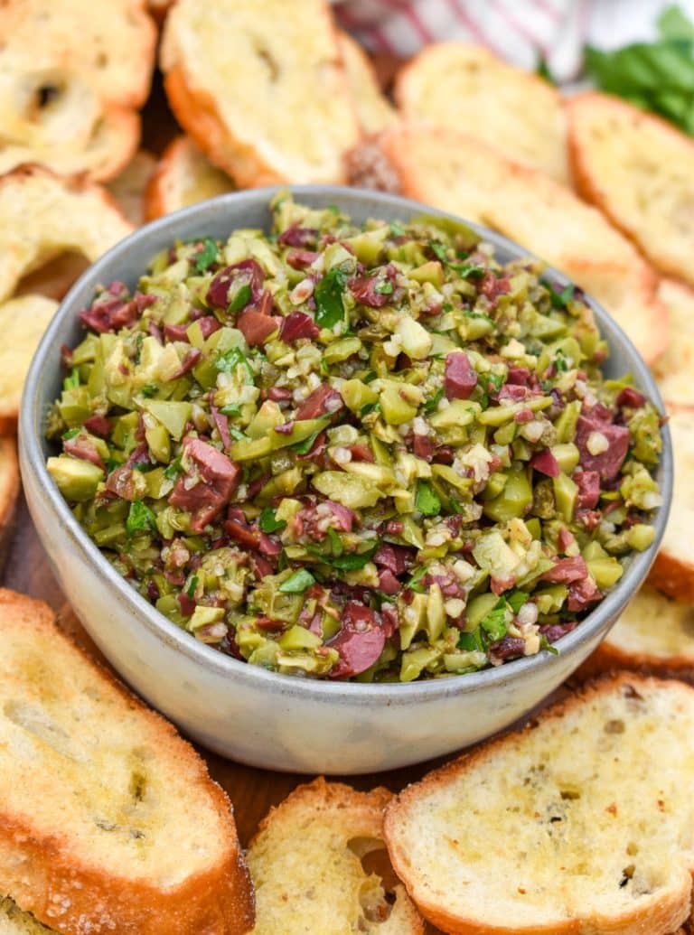 easy homemade olive tapenade in a small gray bowl surrounded by homemade crostini