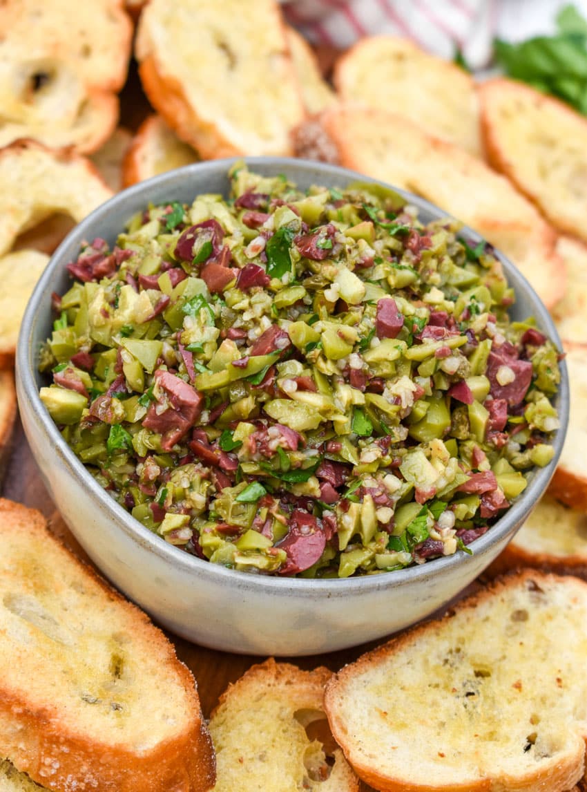 easy homemade olive tapenade in a small gray bowl surrounded by homemade crostini