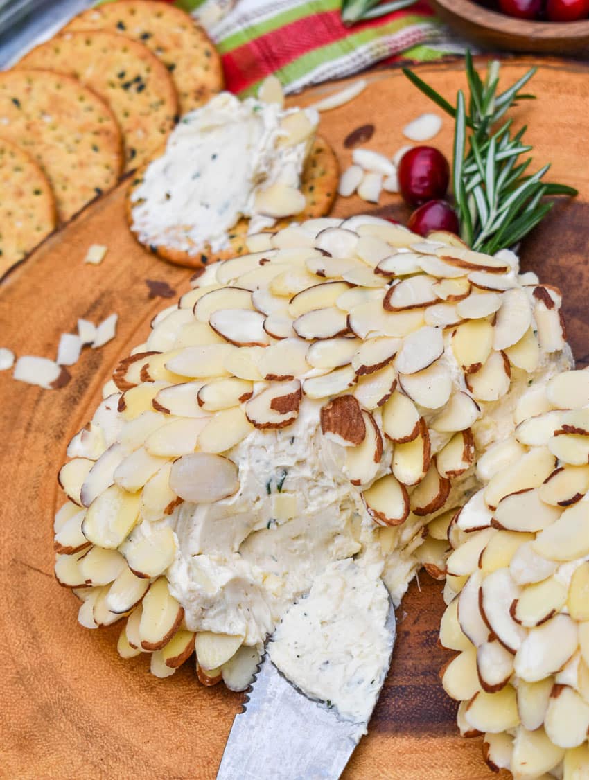 a silver cheese spread digging into a sliced almond covered holiday cheese ball