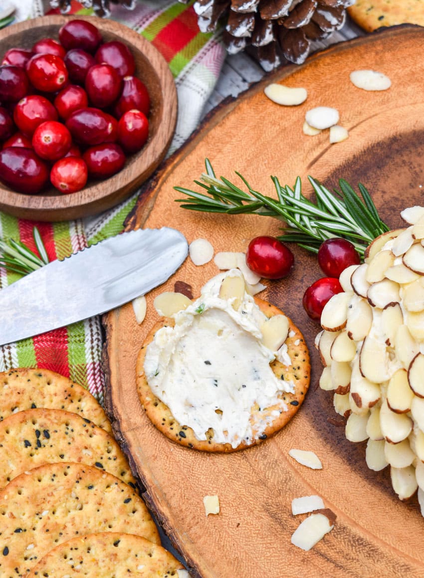 white cheddar cheese ball spread on a multigrain cracker resting on a wooden serving board