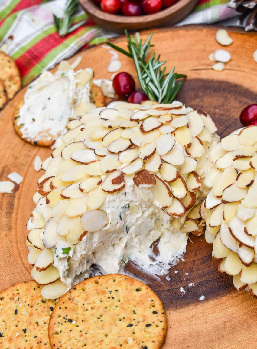 a silver cheese spread digging into a sliced almond covered holiday cheese ball