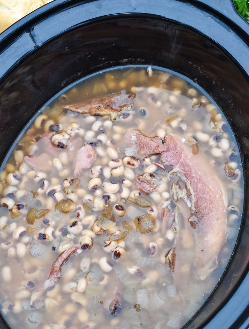 black eyes peas and pieces of leftover ham and onions in broth in the black bowl of a slow cooker