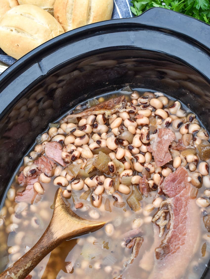 stewed black eyed peas with onions and chunks of ham in the black bowl of a slow cooker