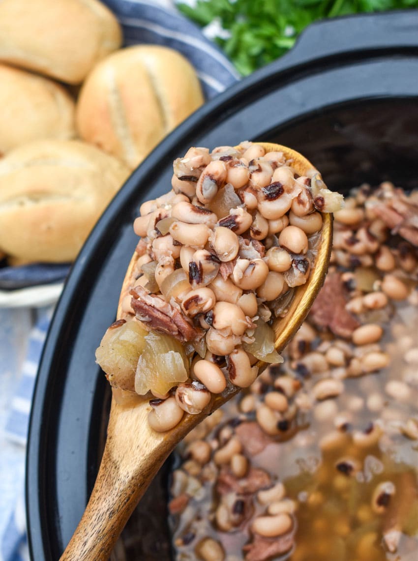 a wooden serving spoon holding up a scoop of slow cooker black eyed peas