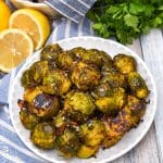smashed brussels sprouts topped with shredded parmesan cheese on a small white plate