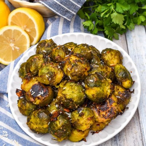 smashed brussels sprouts topped with shredded parmesan cheese on a small white plate