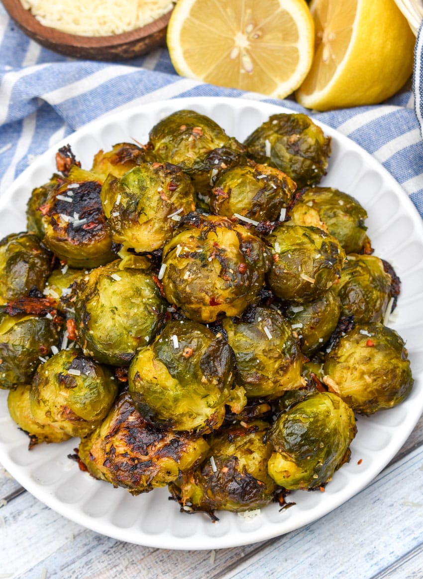 smashed brussels sprouts topped with shredded parmesan cheese on a small white plate