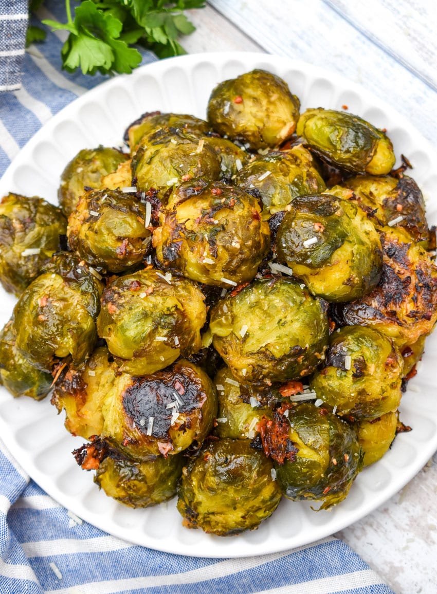 smashed brussels sprouts topped with shredded parmesan cheese on a small white plate